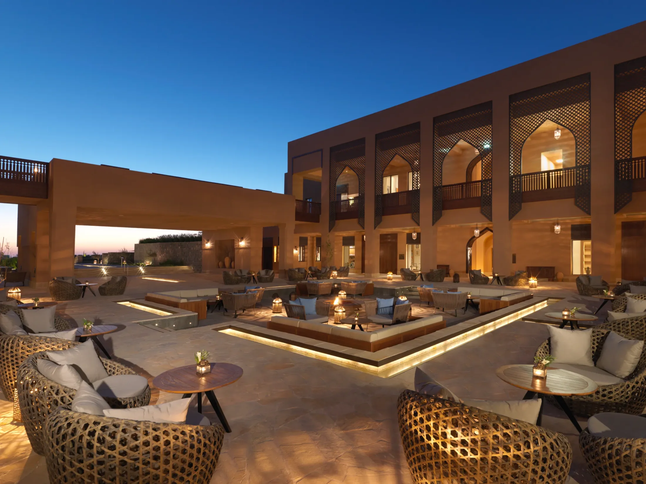 Elegant outdoor lounge area at the Anantara Al Jabal Al Akhdar Resort at sunset with woven chairs and tables.