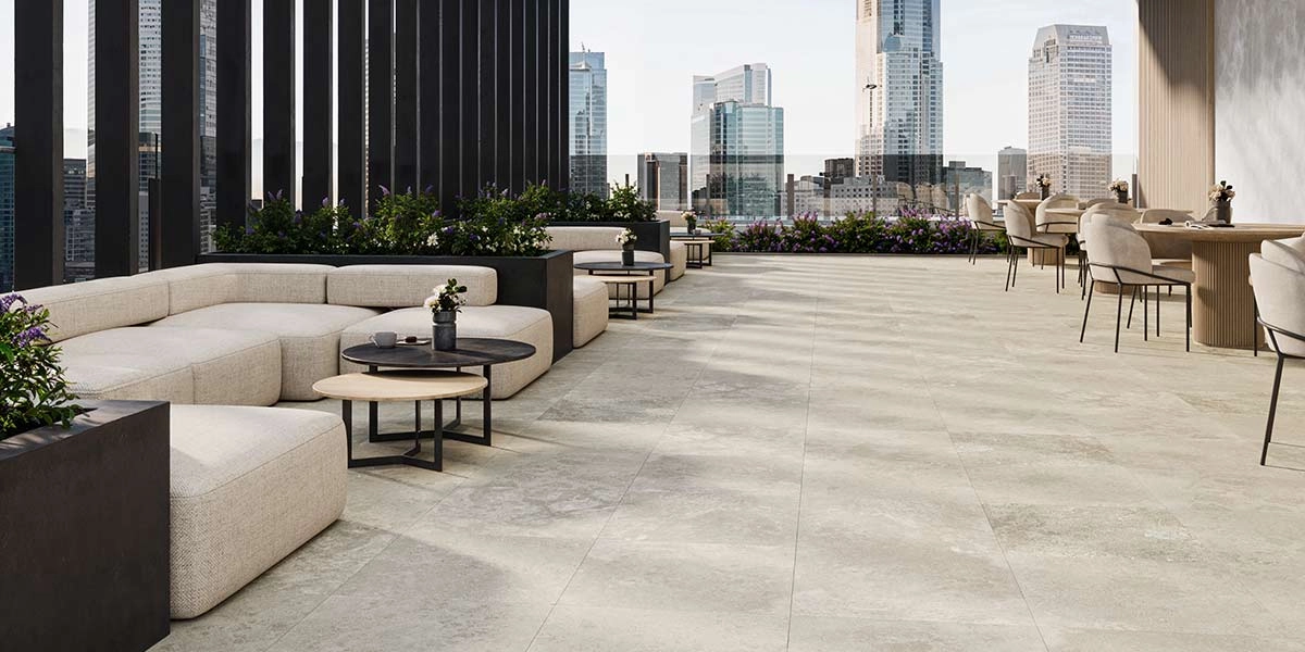 Modern travertine rooftop terrace with beige sectional seating, round tables, and a city skyline view, highlighting the use of travertine to create a luxury terrace.